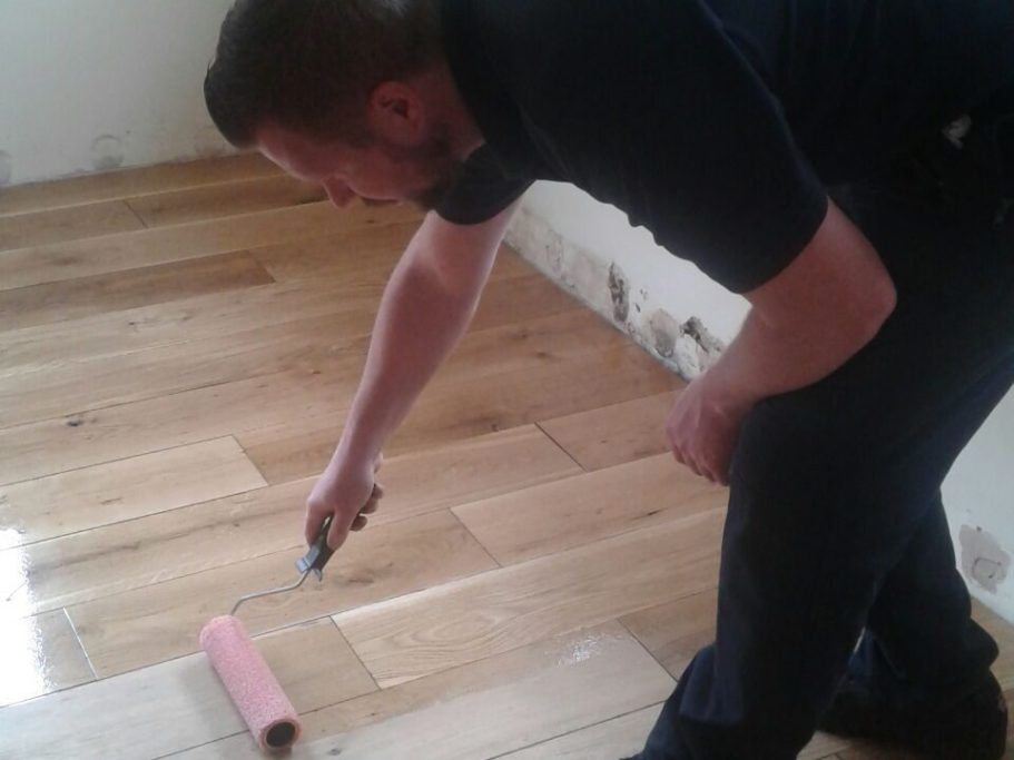 Handyman treating solid oak flooring with varnish after sanding