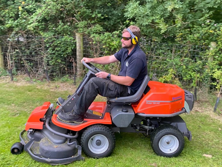 gardener using a ride on mower to cut grass on large paddock